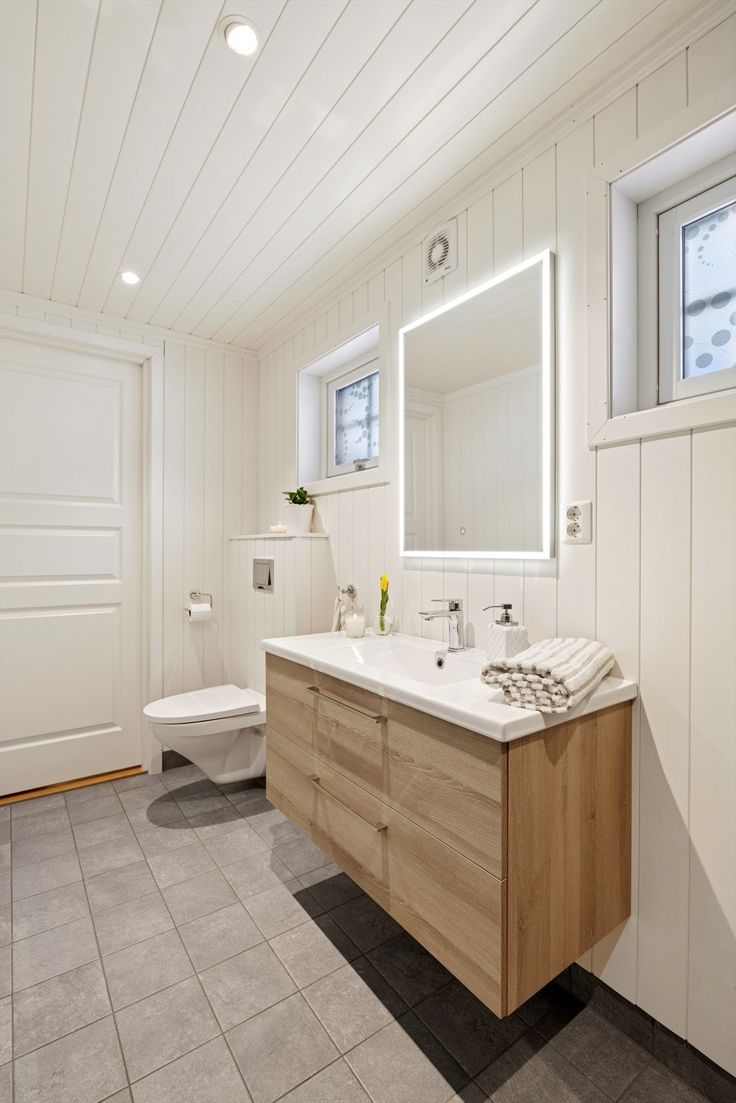 Badet har servant med underskap, speil med tilhørende belysning, høyskap, dusjhjørne og vegghengt wc. Galleribilde