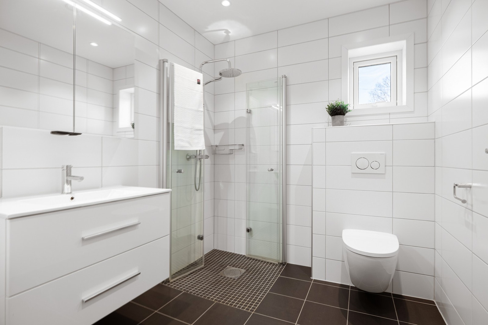 Det er innredet med vegghengt toalett, dusjhjørne med dusjgarnityr og vegger, og baderomsmøblement med speilskap og belysning. Galleribilde