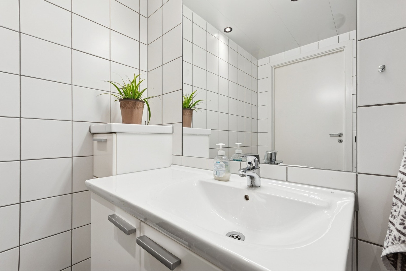 Rommet er innredet med servant i servantskap, wc på vegg, dusj på vegg med dusjvegger og opplegg for vaskemaskin. Galleribilde