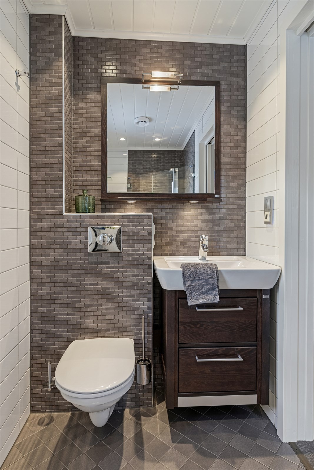 Helfliset bad med varme i gulv. Rommet har dusjhjørne, vegghengt toalett og servant med underskap. Downlights i himling. El. styrt vifte. Badet er etablert i et tidligere toalettrom. Det foreligger ikke dokumentasjon på at endringen er søknadsbehandlet. Galleribilde