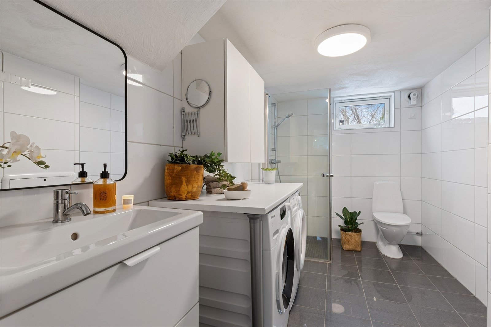 Badet er innredet med fliser på både gulv og vegger, elektriske varmekabler for ekstra komfort, dusjhjørne med dusjvegger, servant med innredning samt opplegg for vaskemaskin. Galleribilde