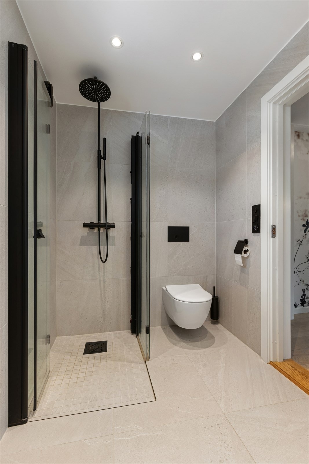 Badet er utstyrt med vegghengt toalett, dusjhjørne med dusjvegger og en elegant servantinnredning. Galleribilde