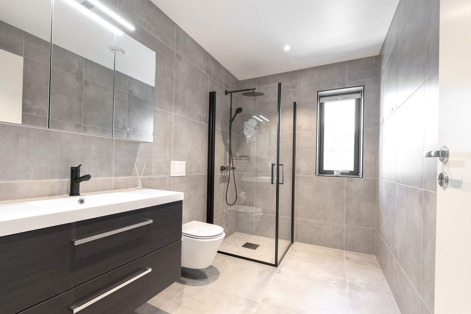 Møbler og sanitærutstyr i samme serie danner en rød tråd mellom boligens to bad. Storformat fliser på gulv og vegger skaper helhet. Galleribilde