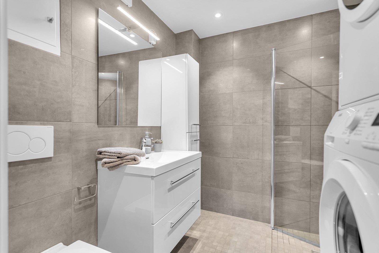 Meget delikat, helfliset baderom fra 2018 som kombinerer stil og funksjonalitet. Badet er innredet med servant og underskuffer, samt matchende baderomsmøbler som gir rikelig med oppbevaringsplass. Galleribilde