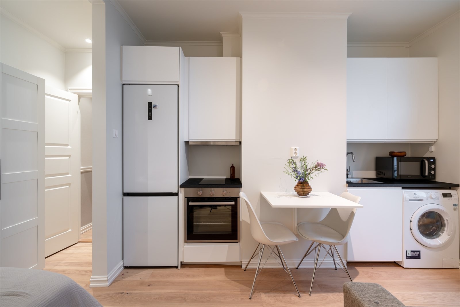 Stilren kjøkkeninnredning med glatte fronter og belysning under overskap. Kullfilterventilator, stekeovn og platetopp er integrert i innredning. Det er opplegg for vaskemaskin Galleribilde