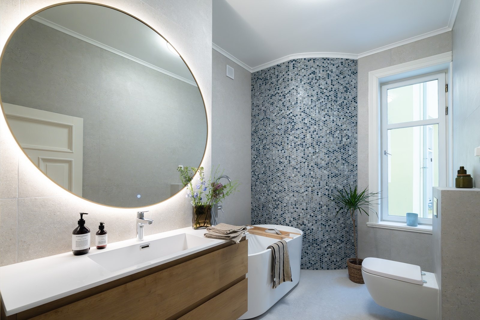 Moderne innredning bestående av benkeskap, servant med speil, dusjløsning i badekar og vegghengt toalett med innebygget sisterne Galleribilde