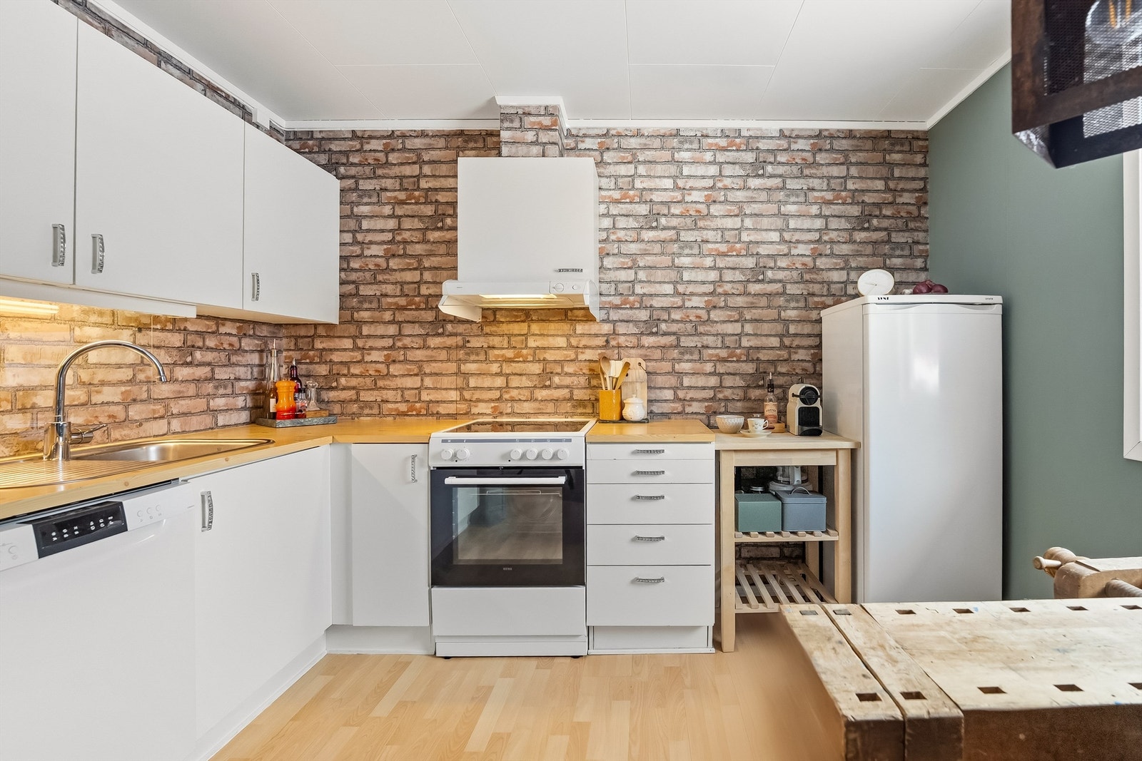 Det er benkeplate med laminert overflate, nedfelt kjøkkenvask med armatur, benkeskapsbelysning og stikkontakter over kjøkkenbenk, frittstående komfyr (fra 2023), oppvaskmaskin og kjøleskap. Galleribilde