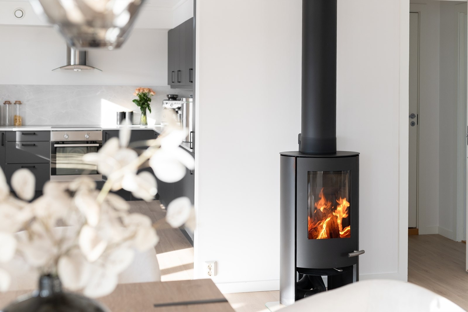 Sentralt i rommet står en moderne vedovn med glassfront, som gir lun varme og skaper en hyggelig atmosfære. Galleribilde