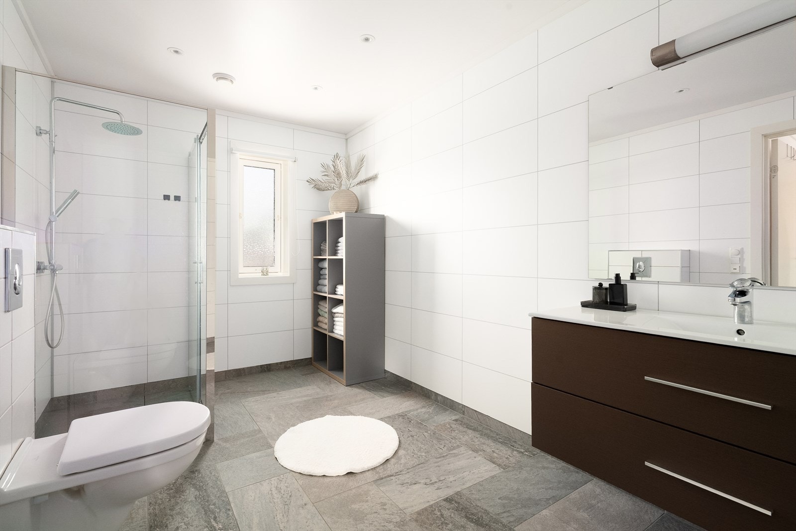 Stort og lyst bad nede, med flislagt gulv og våtromsplater på vegger. Varmekabler i gulv, veggmontert toalett og innglasset dusjhjørne. Galleribilde