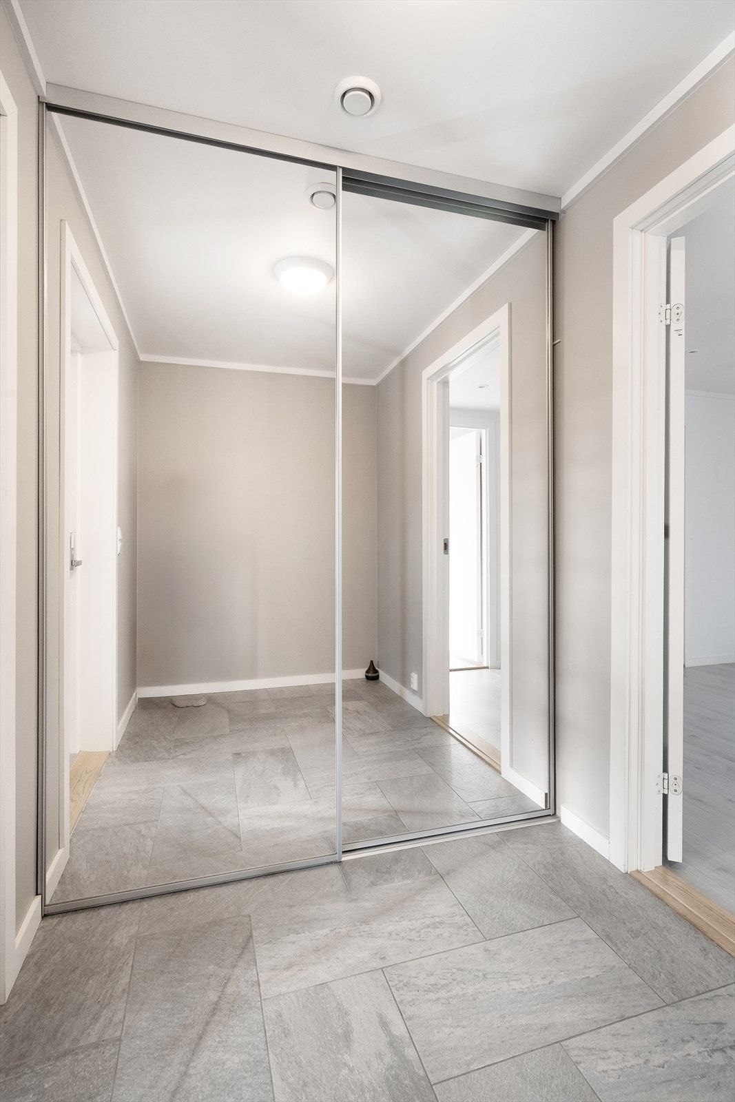 Fin og romslig entré med flislagt gulv og varmekabler. Praktisk skyvedørsgarderobe med god plass til skjult oppbevaring av sko- og yttertøy. Galleribilde