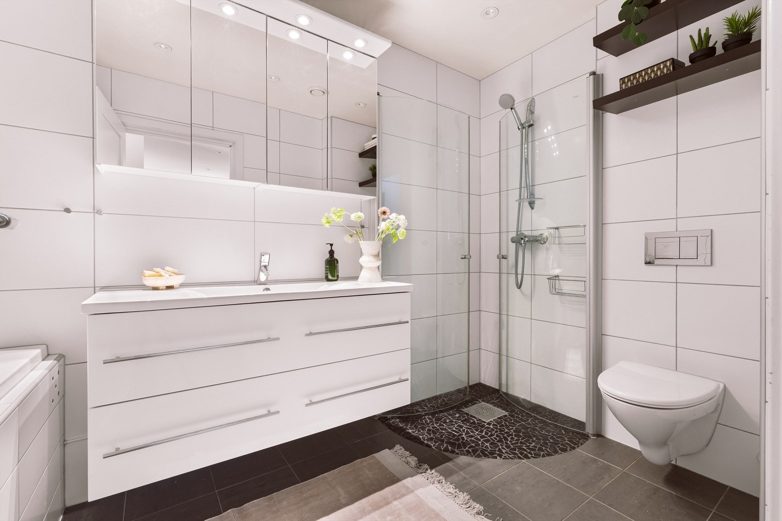 Innredningen består av nedfelt servant med underskap, speilskap, vegghengt toalett, dusjsone og innebygd badekar. Galleribilde