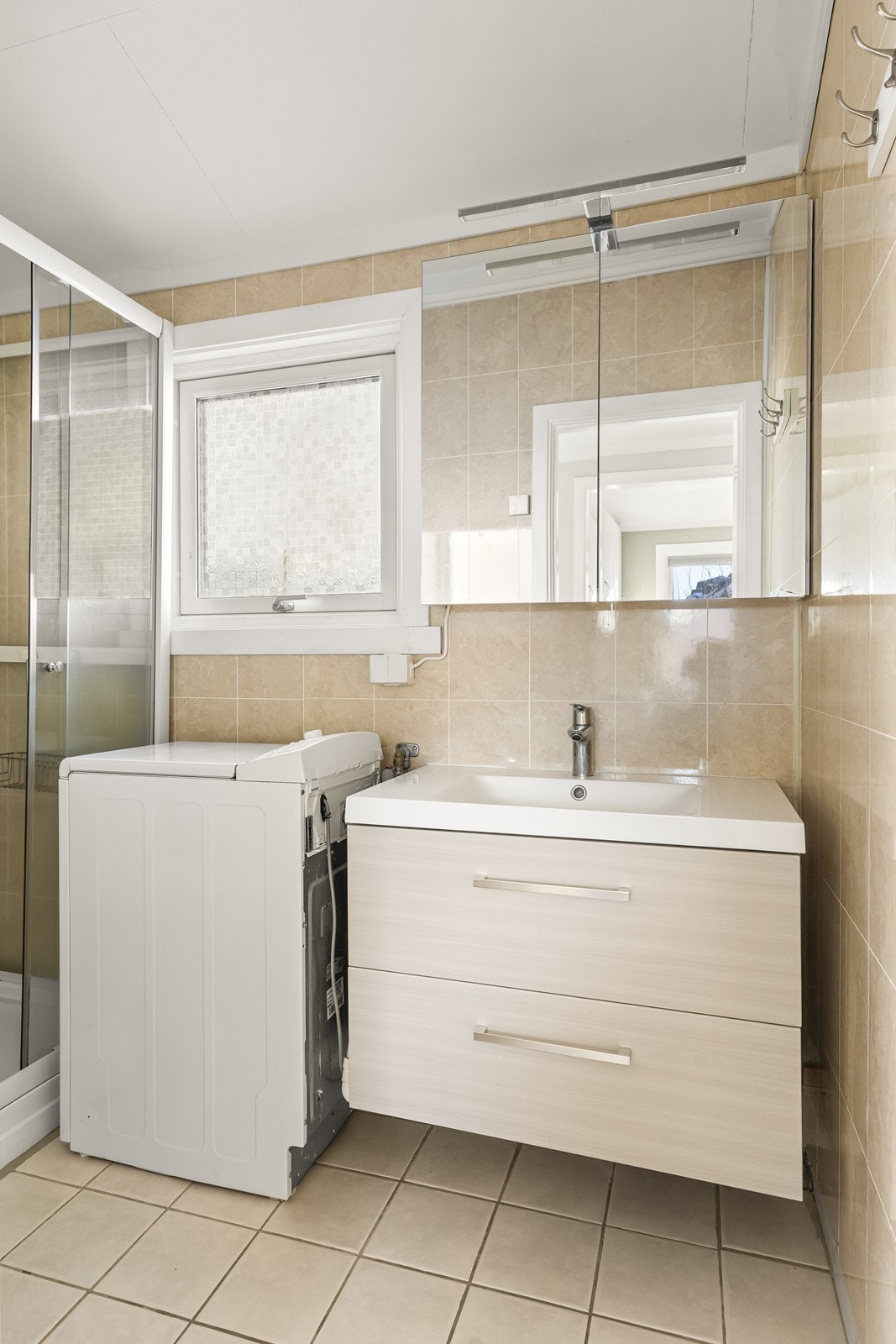 Badet har flislagt gulv med gulvvarme, servantinnredning med skuffer og opplegg for vaskemaskin. Galleribilde