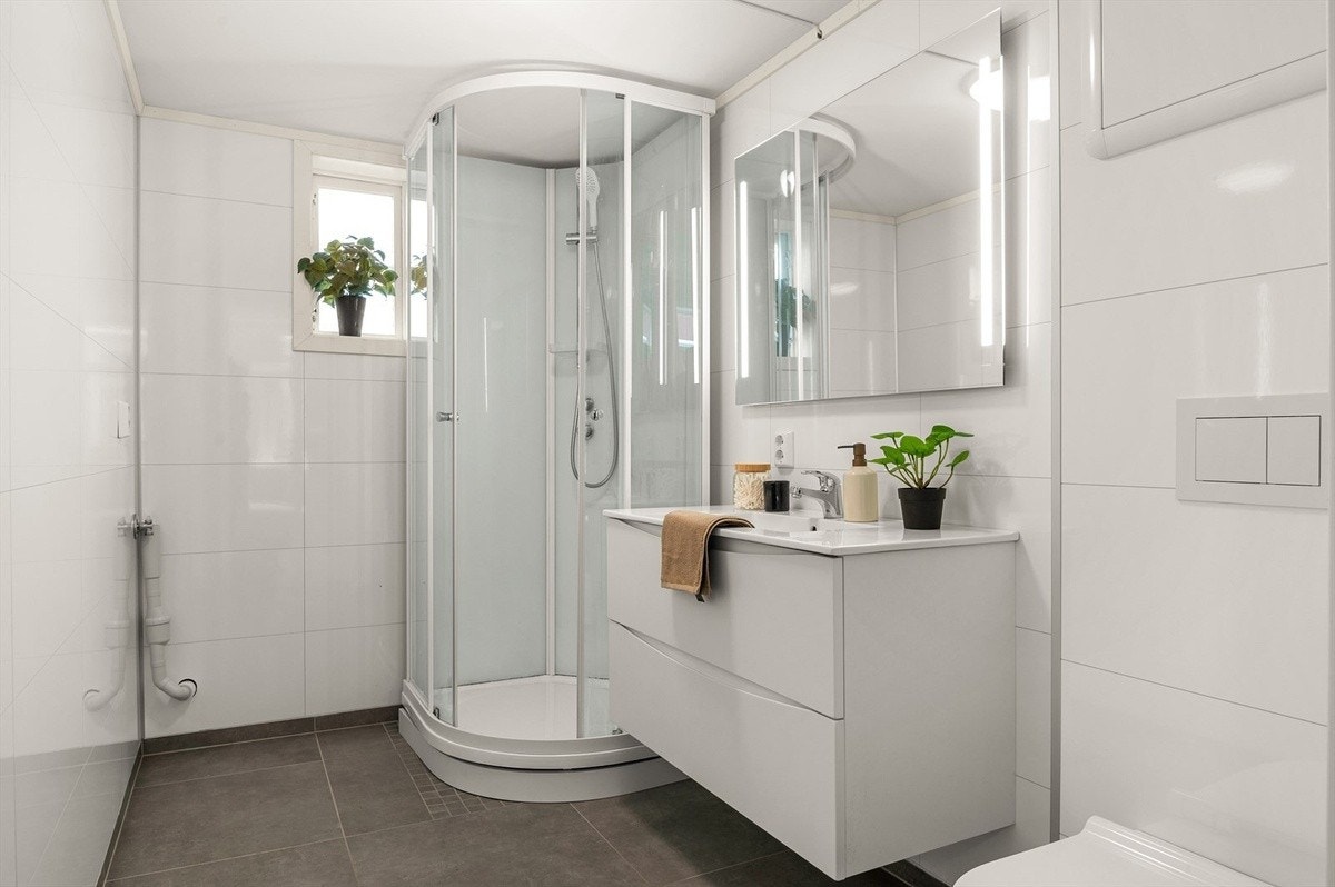 Badet er på 5 kvm og er praktisk innredet med veggmontert wc, servant med underskap for oppbevaringsplass og dusjkabinett som skåner vann direkte på gulvflisene. Badet har opplegg for vaskemaskin og gulvvarme. Galleribilde