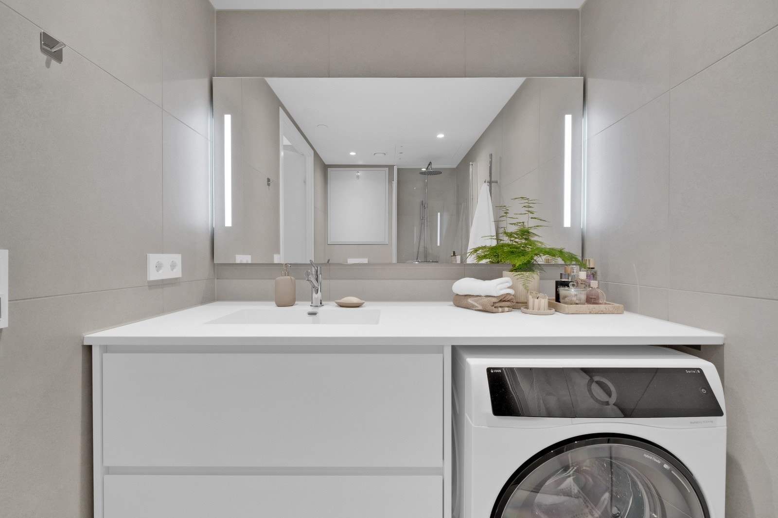 Badet er utstyrt med stilren, hvit baderomsinnredning med praktisk skuffeoppbevaring, servant og speil med integrert belysning. I tillegg har badet dusj med innfellbare dusjdører samt vegghengt toalett Galleribilde