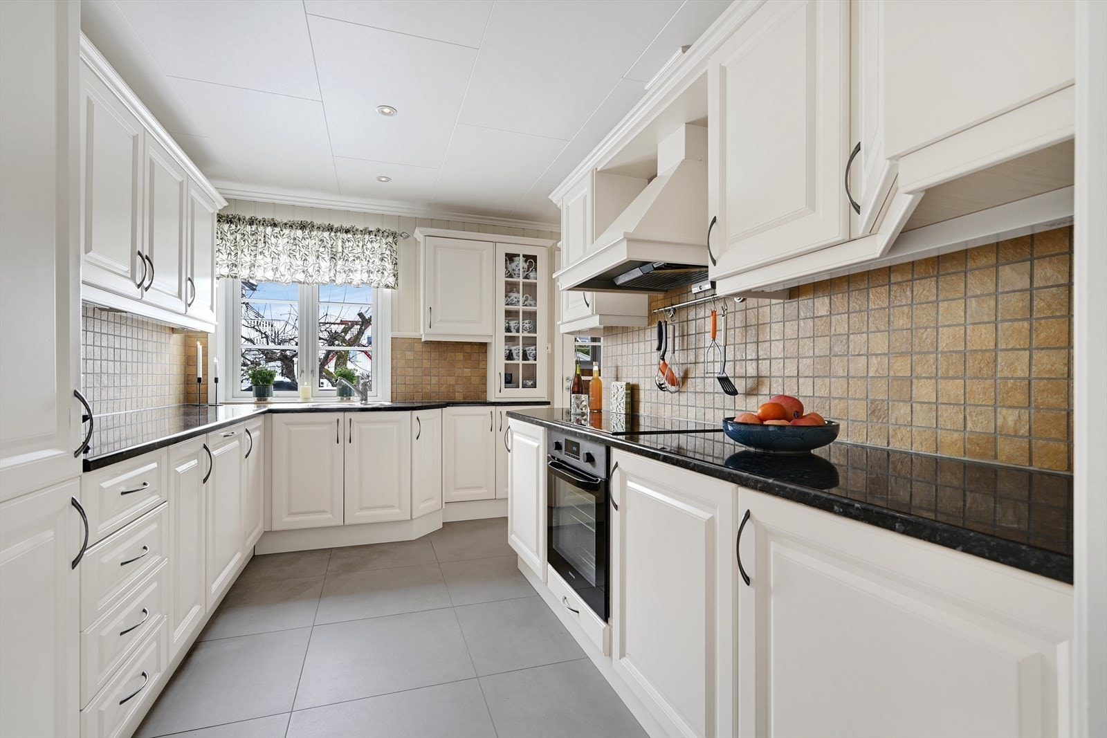 Velutstyrt kjøkken med profilerte fronter og fliser mellom benk og overskap. Galleribilde