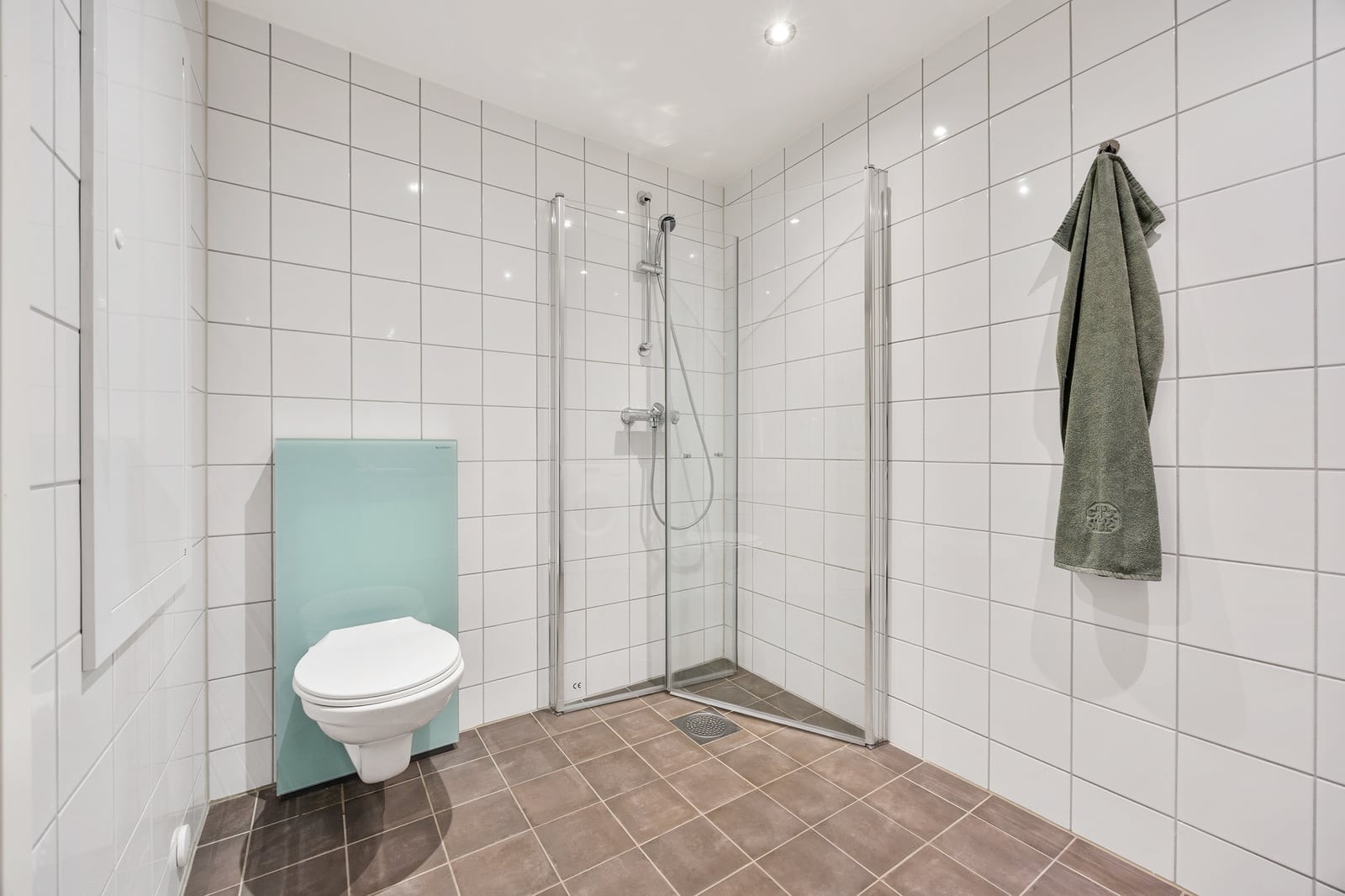 Dusjhjørne med inn- og utadslående dører i herdet glass og vegghengt toalett. Galleribilde