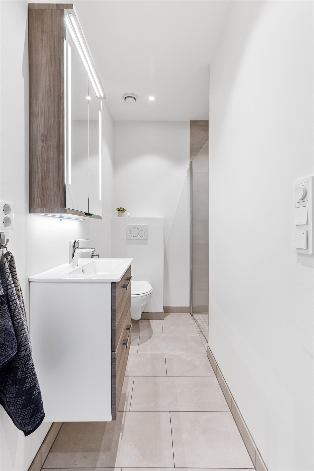 Baderom fra byggeår. Flislagt gulv med gulvvarme. Malte og flislagte veggflater. Malte flater i himling. Vegghengt servantinnredning. Speil med sidelys. Galleribilde