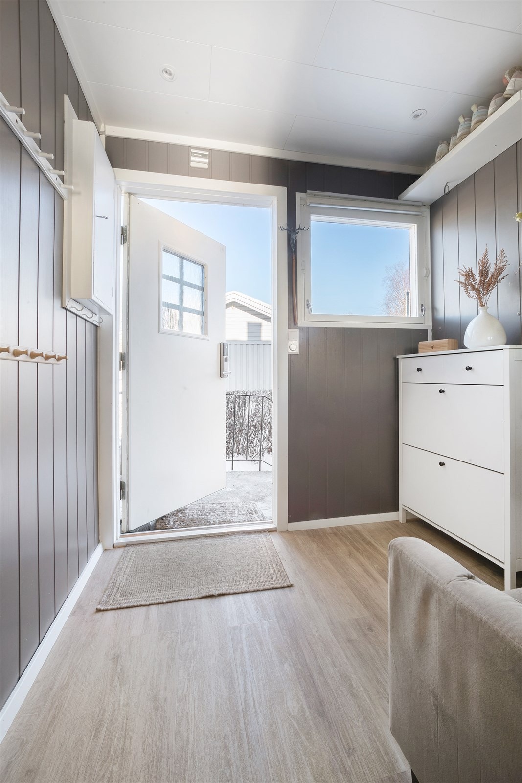 Man kommer inn i en lys entré med laminat på gulv og malt panel på veggene Galleribilde