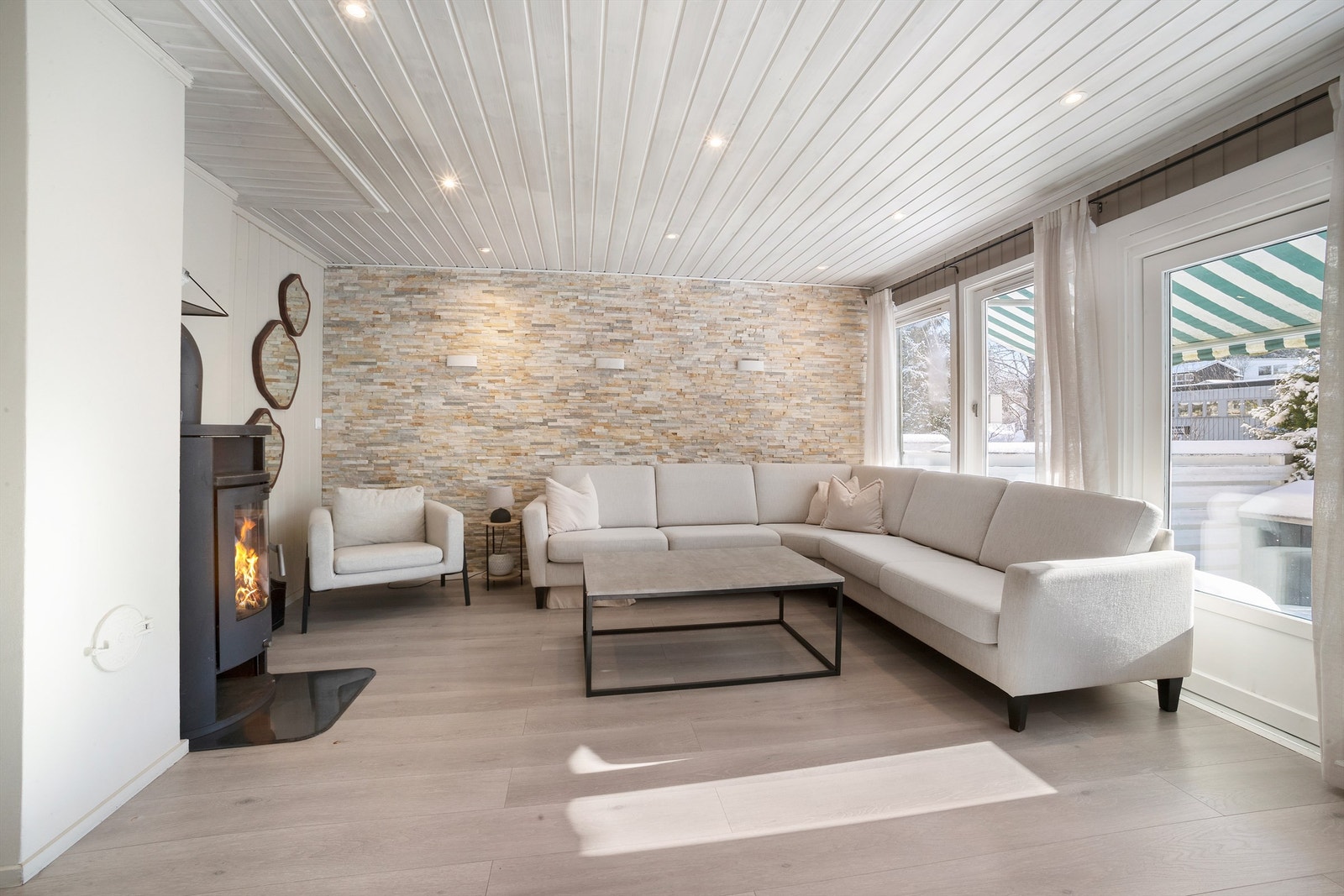 Lys og fin stue med gulv belagt med laminat og vegger av stående panel, samt en dekorativ fondvegg av skifer Galleribilde