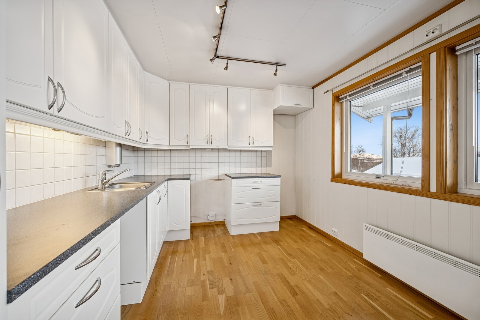 Velholdt kjøkken med hvite fronter og god oppbevaringsplass. To vinduer sørger for et lyst og trivelig arbeidsrom Galleribilde