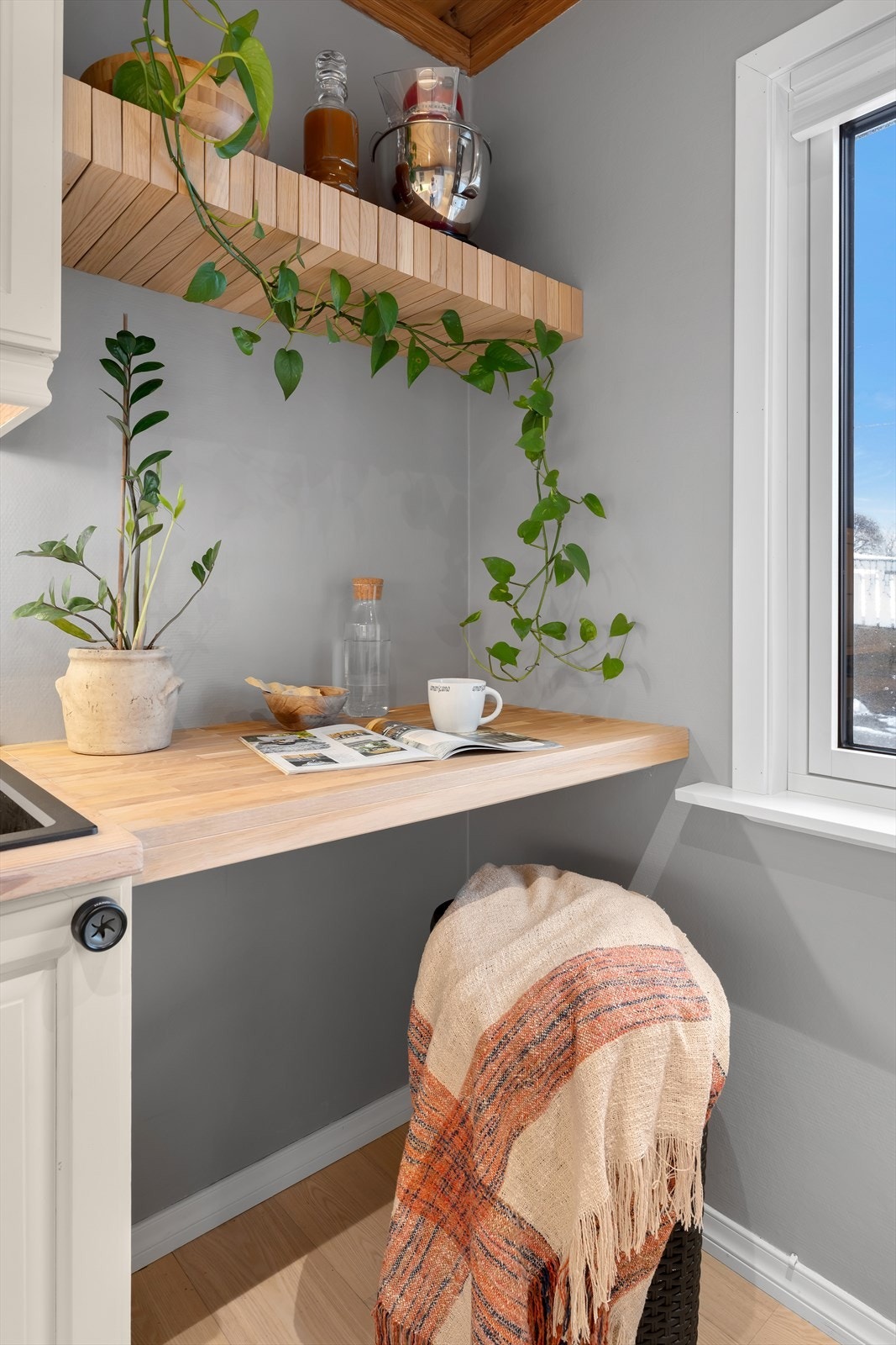 Det er også satt opp en ekstra plate mellom kjøkkeninnredningen og vinduet, som fungerer som en praktisk og hyggelig sitteplass. Over sitteplassen er det montert stilige hyller, som tilfører både funksjonalitet og estetikk til kjøkkenet. Galleribilde