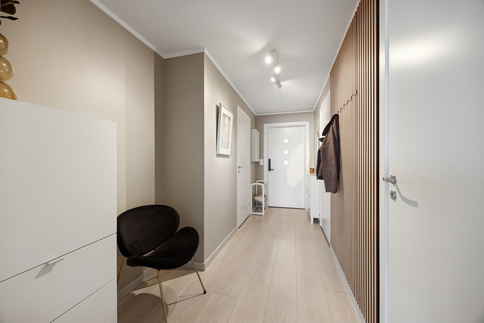 Du ønskes velkommen inn i en lys og trivelig entré med plass til å sette fra seg sko og henge yttertøy. En moderne spilevegg med knagger gir en praktisk og stilren oppbevaringsløsning Galleribilde