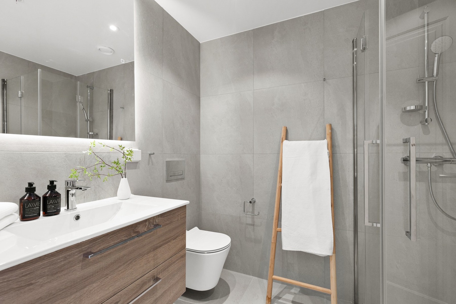 Lekkert baderom utstyrt med downlights, varmekabler, vegghengt toalett, dusjhjørne og servant samt speil. Galleribilde