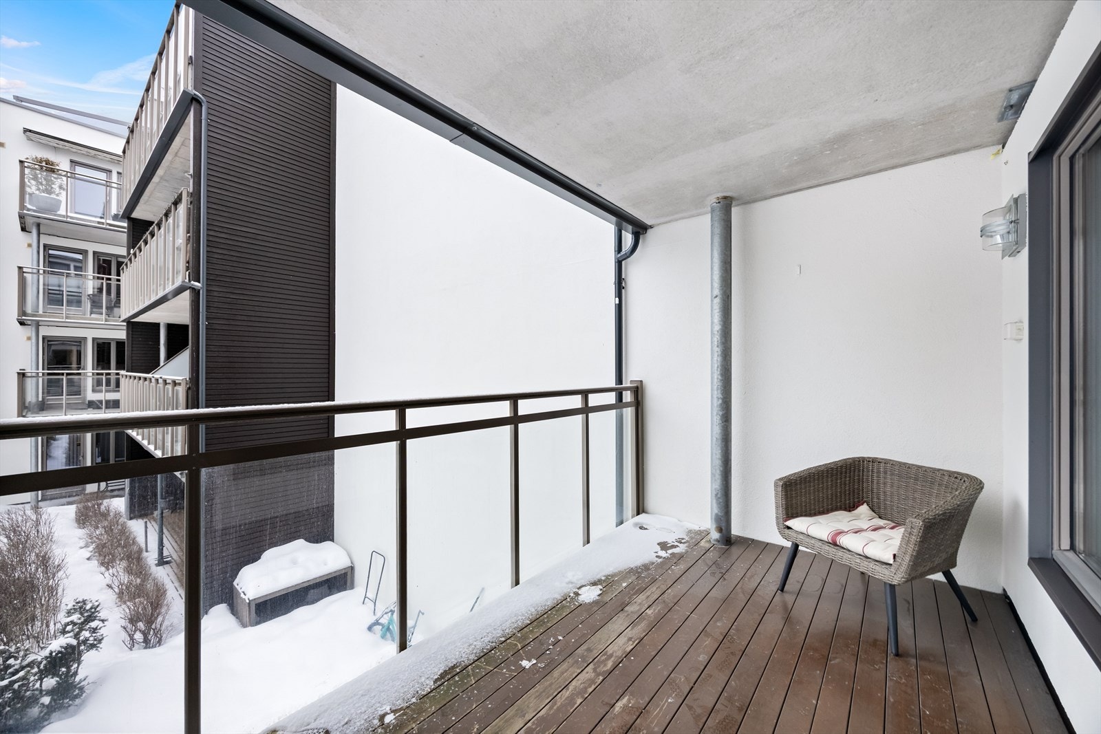 Balkongen har takoverbygg, rekkverk med glassfelt og tredekke. Utebelysning og stikk på vegg. Galleribilde