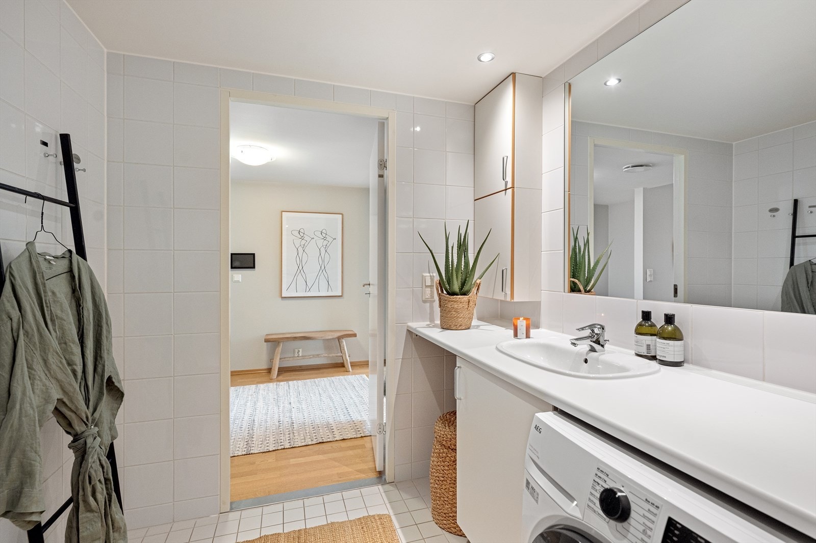 Badet er innredet med veggfestet toalett, servant, dusj på gulv med dører i herdet glass og opplegg for vaskemaskin. Galleribilde