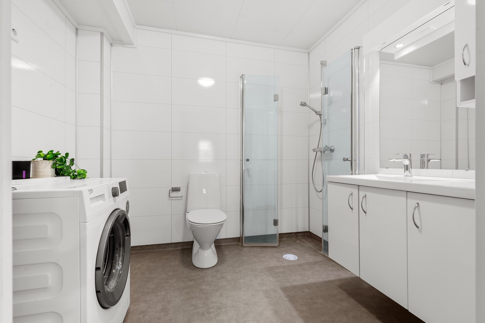 Badet inneholder servantinnredning med god skapplass, dushjørne med innfellbare dører, toalett, røropplegg for vaskemaskin og skyllekar Galleribilde