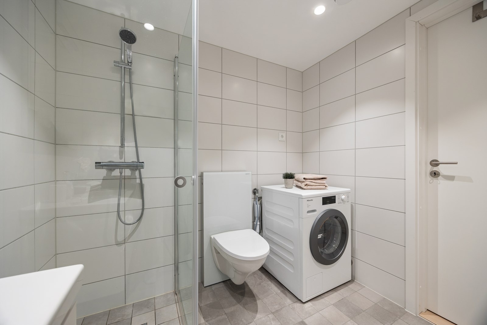 Rommet er utstyrt med servant, vegghengt toalett, dusjhjørne og opplegg for vaskemaskin og tørketrommel. Galleribilde