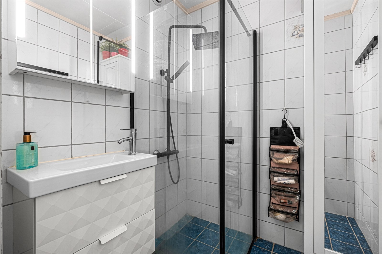 Badet er flislagt og utstyrt med dusjkabinett, servant med over og underskap samt vegghengt oppbevaring, en arealeffektiv løsning på 2,6 m². Galleribilde