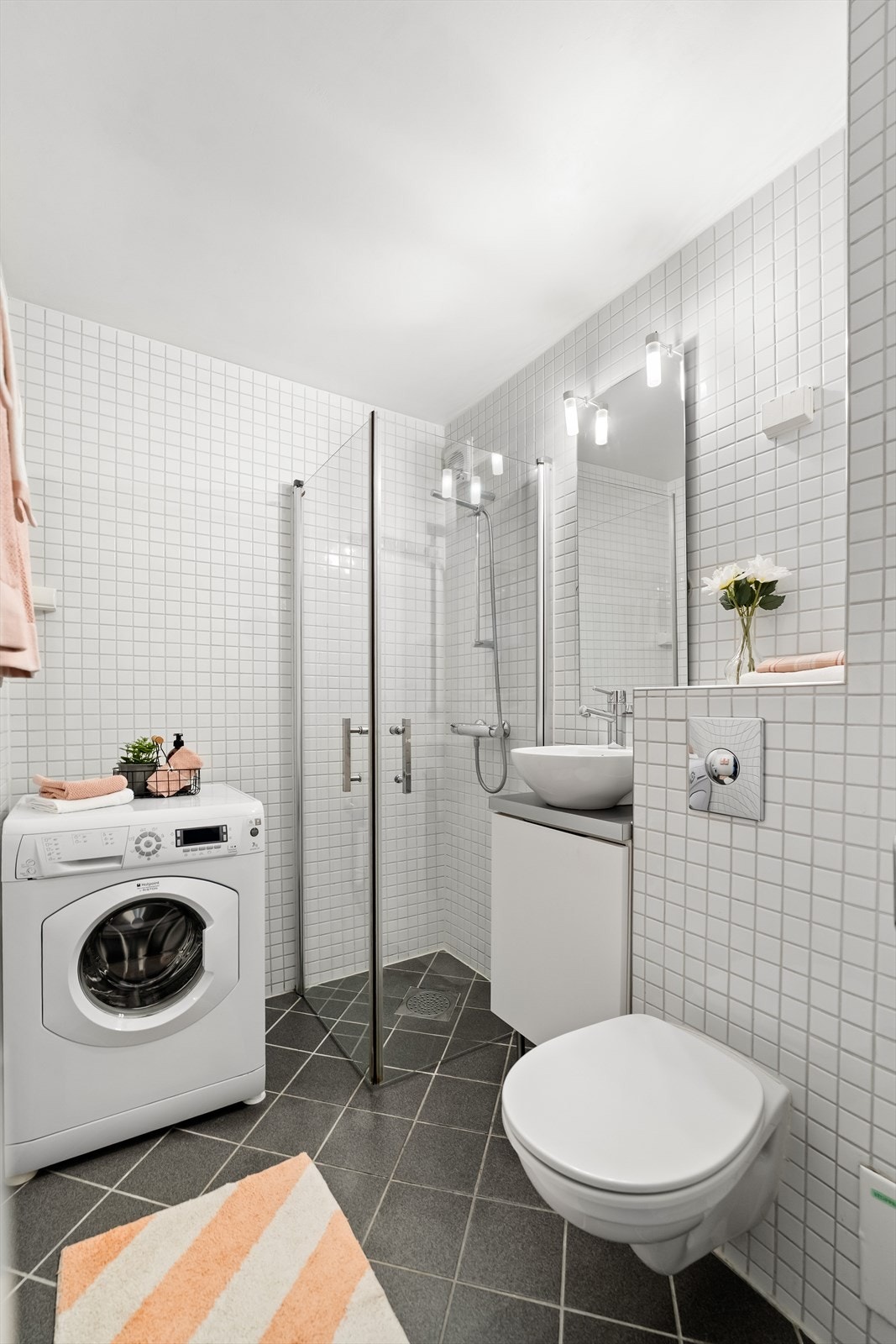 Badet er innredet med veggmontert toalett, dusj med herdet glassdører, baderomsinnredning med finert front og laminat benkeplate med overliggende servant, samt veggspeil med belysning. Det er opplegg for vaskemaskin, noe som gjør hverdagen enkel. Galleribilde