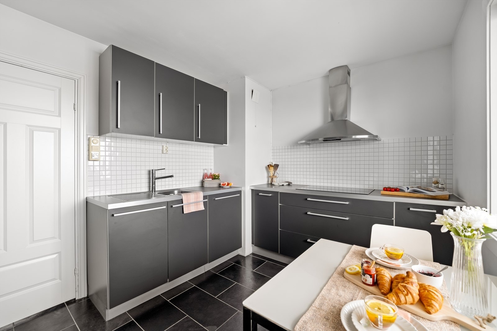 Kjøkkenet har en stilren innredning med finerte, mørkegrå fronter og laminat benkeplate, kombinert med fliser over benk som gir et helhetlig uttrykk. Galleribilde