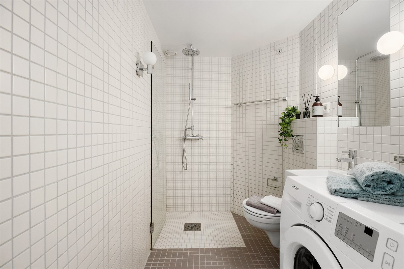 Lyst og flislagt bad med veggmontert WC, regndusj, servant og opplegg for vaskemaskin. Galleribilde