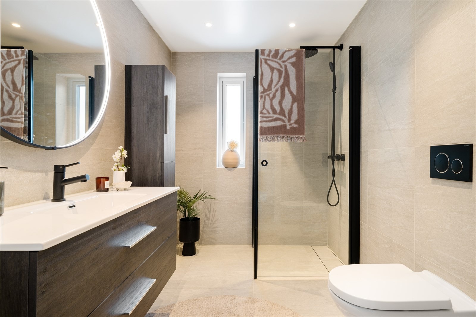 Meget lekkert baderom med flislagte gulv og veggflater. Stor og praktisk baderomsinnredning som videre er supplert med vegghengt høyskap. Sorte detaljer, regnfallsdusj og linjesluk Galleribilde