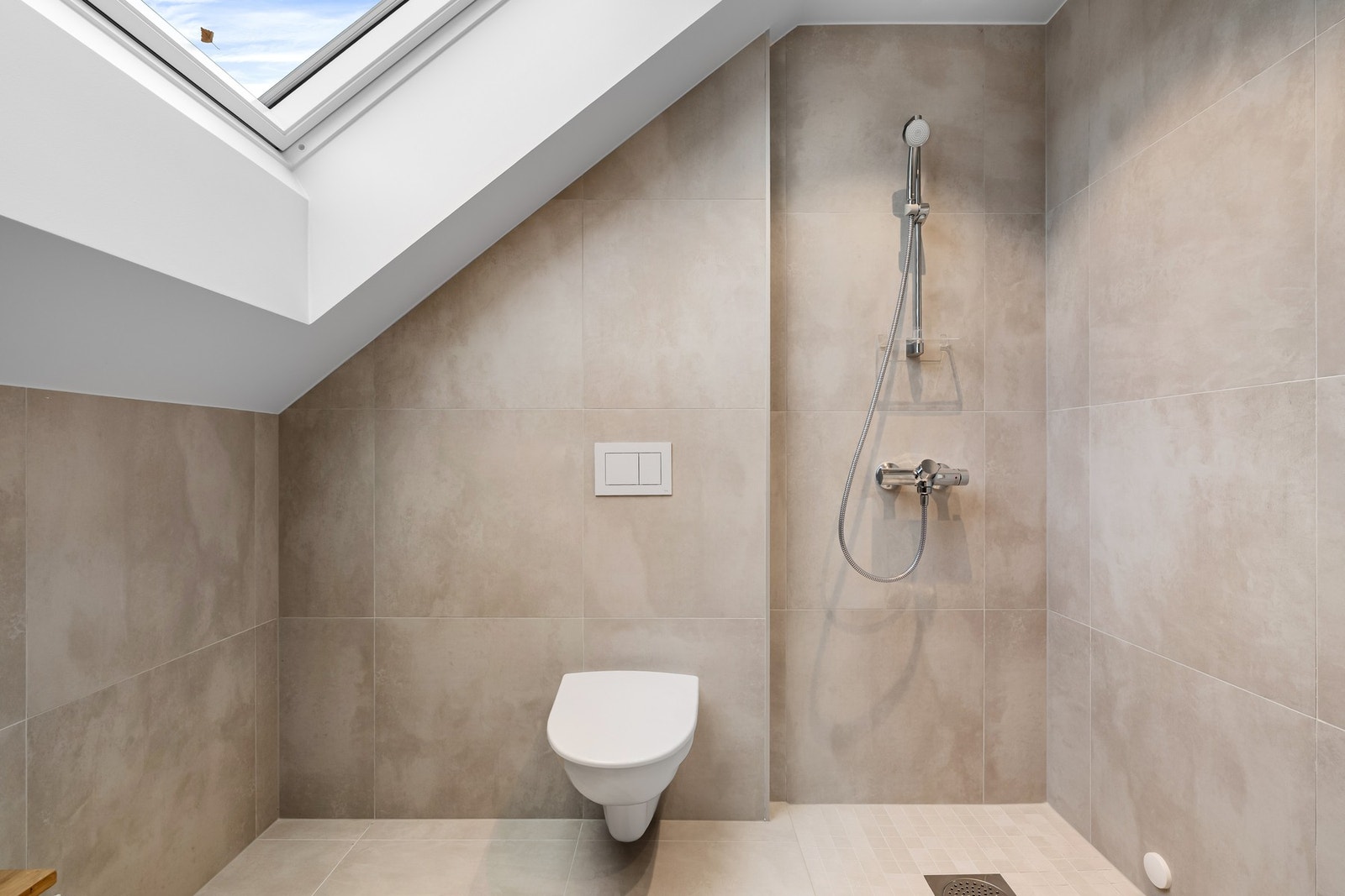 Romslig dusjhjørne med takvindu og vegghengt toalett. Bildene er fra naboleilighet (15B), med identiske løsninger og materialvalg. Galleribilde