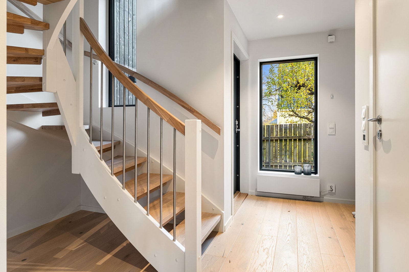 Lys entré med åpen trappeløsning og store vinduer - gir et godt førsteinntrykk og plass til garderobe eller dekor. Bildene er fra naboleilighet (15B), med identiske løsninger og materialvalg. Galleribilde