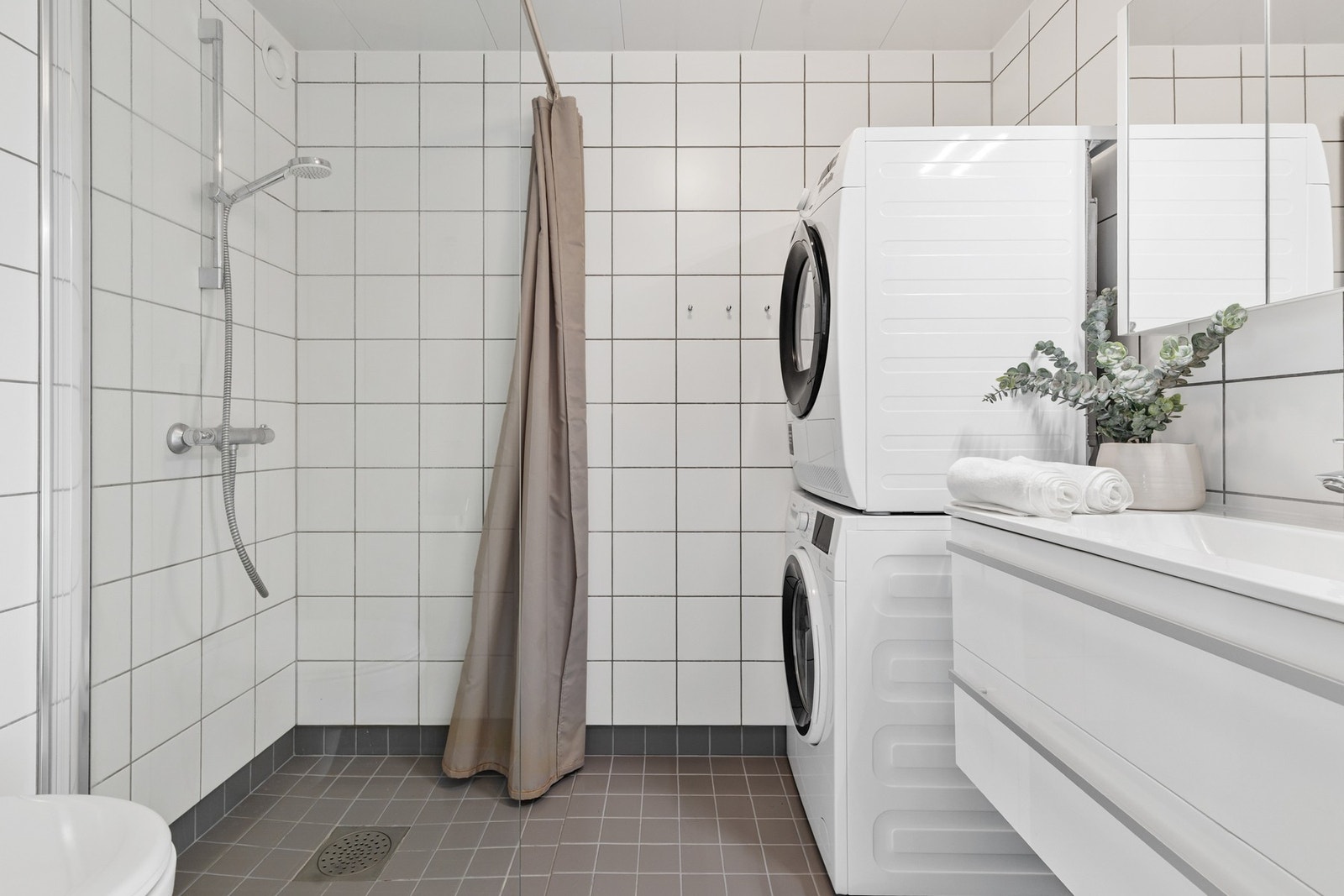 Kombinert bad/vaskerom med fliser på gulv og vegger og takplater i himling Galleribilde