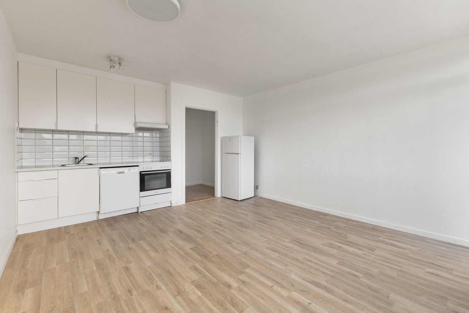 Kjøkkeninnredning med glatte fronter og laminat benkeplate, frittstående hvitevarer som oppvaskmaskin og komfyr. Galleribilde