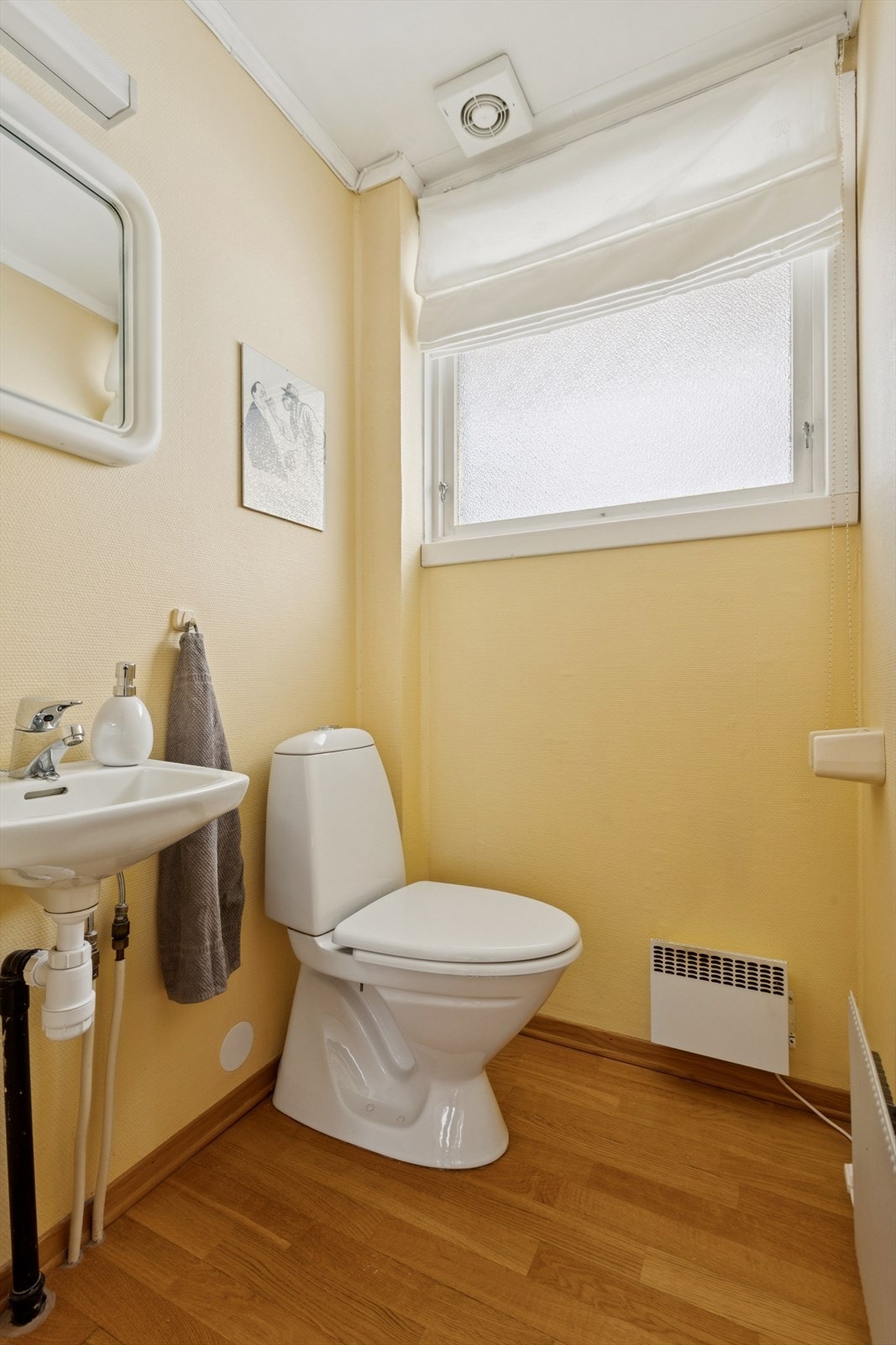 Toalettrommet fremstår som et praktisk og pent rom med parkett på gulvet, malt strie på veggene og takplater i himlingen. Servant, speil med belysning og toalett. Galleribilde