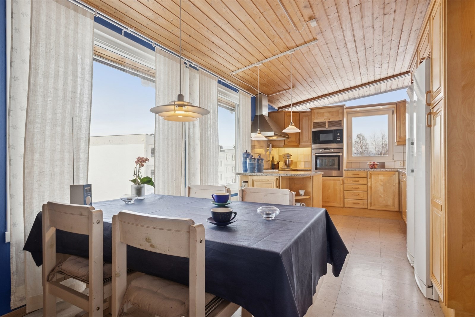 Mot spiseplassen ligger en praktisk kjøkkenøy som gir ekstra benkeplass og en naturlig overgang mellom kjøkken og spiseområde. Flislagt vegg og belysning under overskapene sørger for godt arbeidslys og en behagelig helhet. Galleribilde