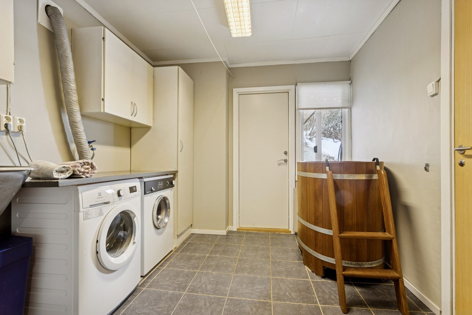 Vaskerommet har høyskap, overskap, utslagsvask i stål og opplegg for vaskemaskin og tørketrommel. Benkeplaten gir praktisk arbeidsflate, og rommet har naturlig avtrekk etter at avtrekket til tørketrommelen ble fjernet. Galleribilde