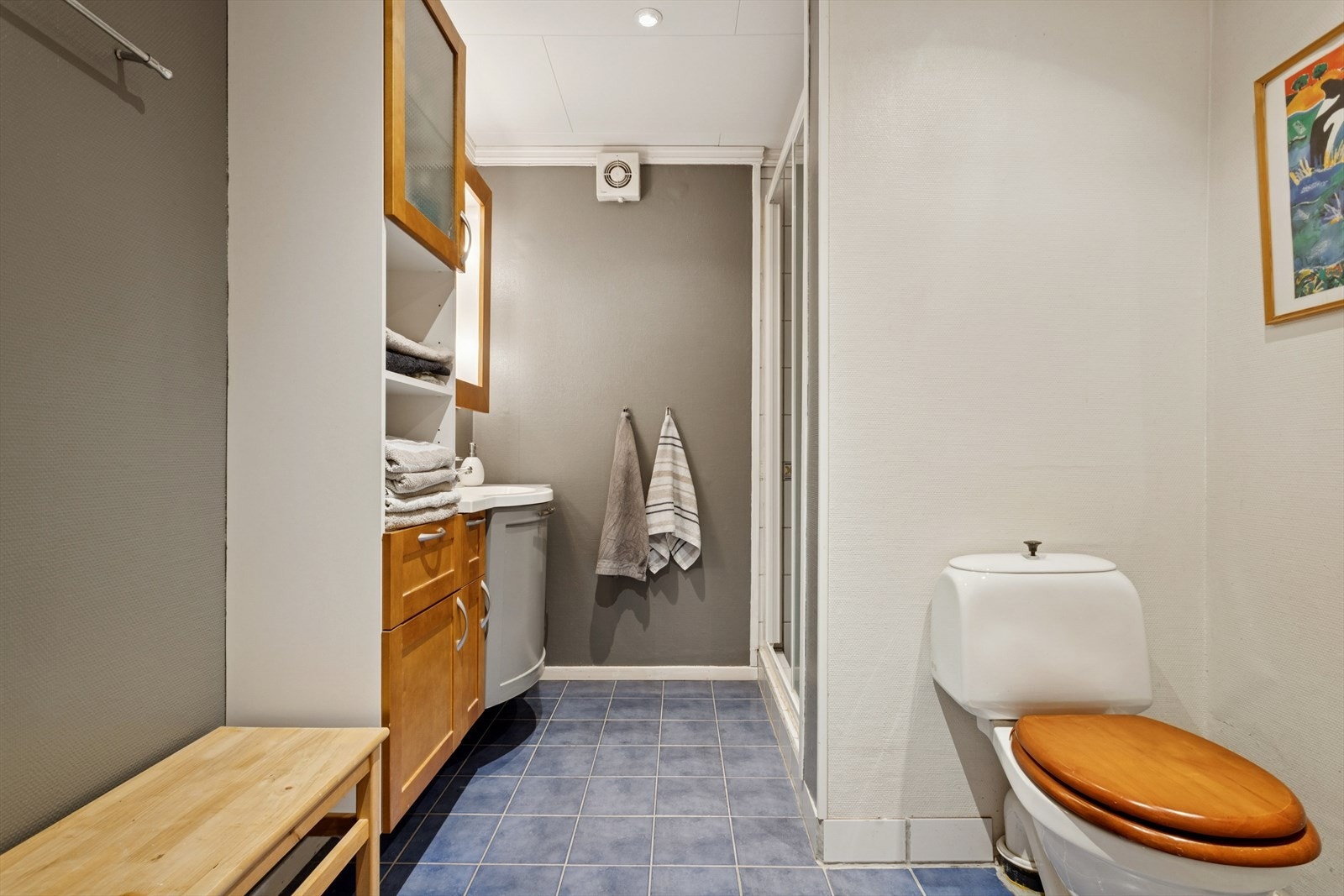 Badet i underetasjen er opprinnelig fra byggeåret, men ble delvis oppgradert rundt år 2000 og fremstår i dag som et funksjonelt og romslig baderom. Gulvet er flislagt og har elektrisk gulvvarme som gir god komfort Galleribilde