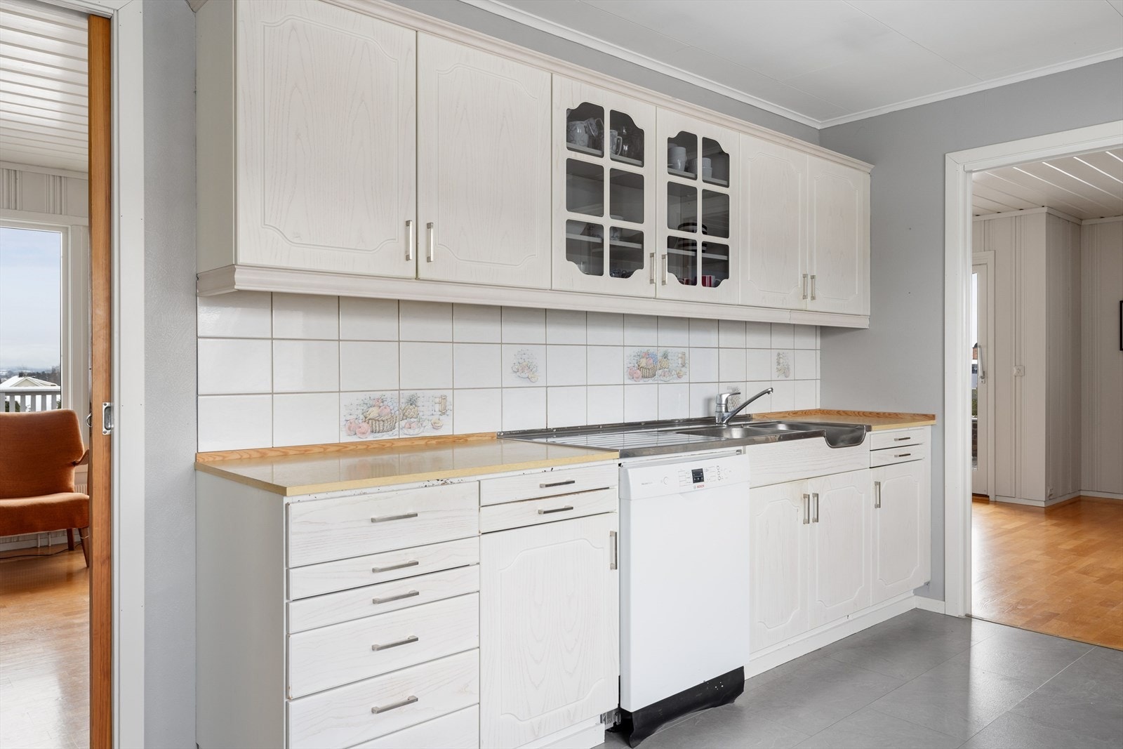 Laminerte benkeplater med benkebeslag med dobbel oppvaskkum I benkeryggen er det fliser. Kjøkkenet har plass til frittstående hvitevarer som oppvaskmaskin, komfyr og kjøleskap. Galleribilde