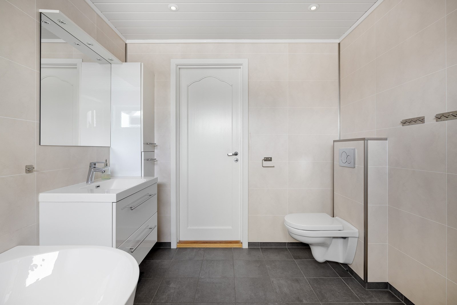 Pent bad i 1. etasje med flislagt gulv med varmekabler og baderomsplater på veggene. I himlingen er det downlights. Galleribilde