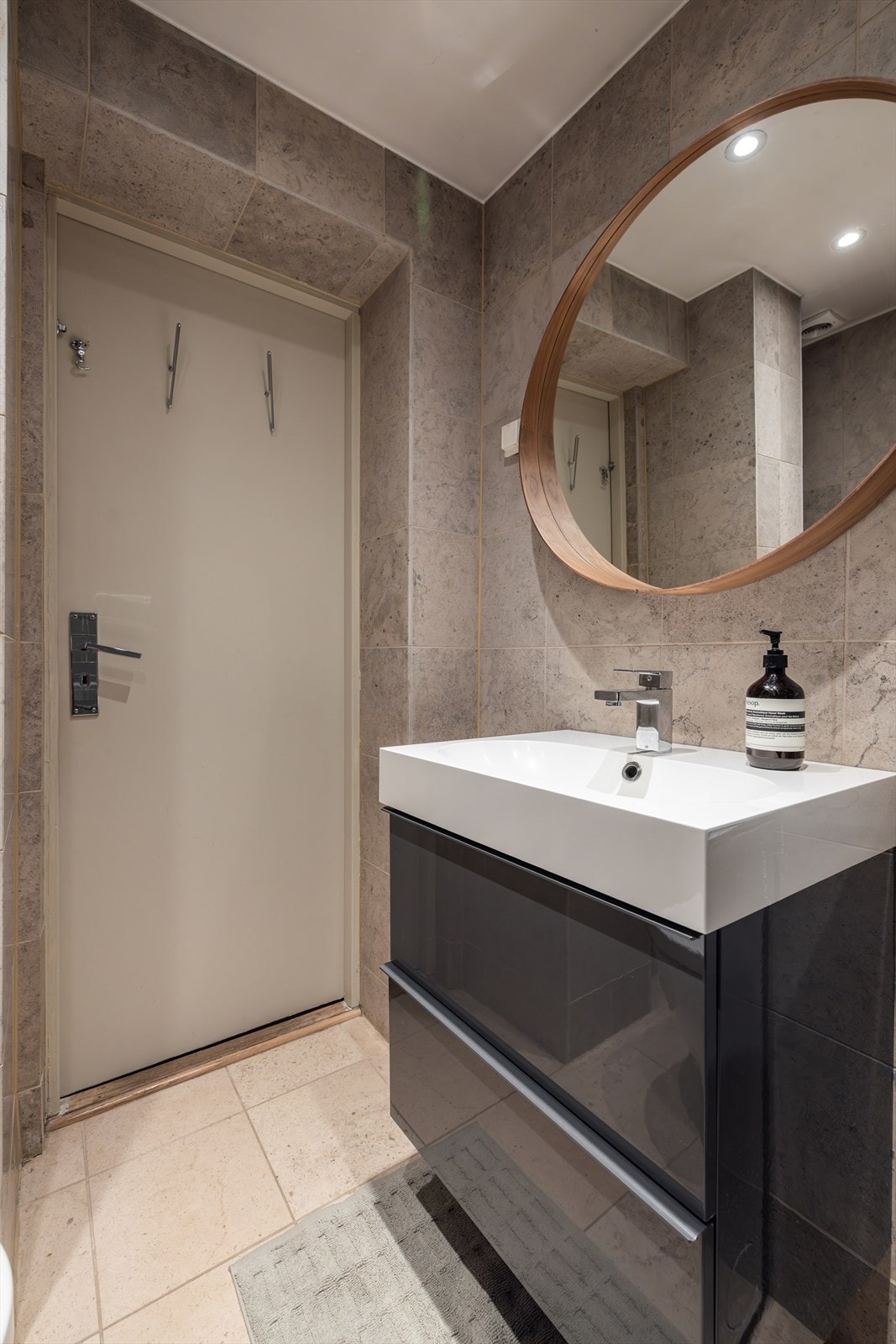 Innredning med servantseksjon med skuffeoppbevaring. Over servanten er det montert rundt speil. Dusjsonen er etablert i nedsenket dusjnisje med glassdører og veggmontert blandebatteri. Videre er det vegghengt toalett og opplegg for vaskemaskin Galleribilde