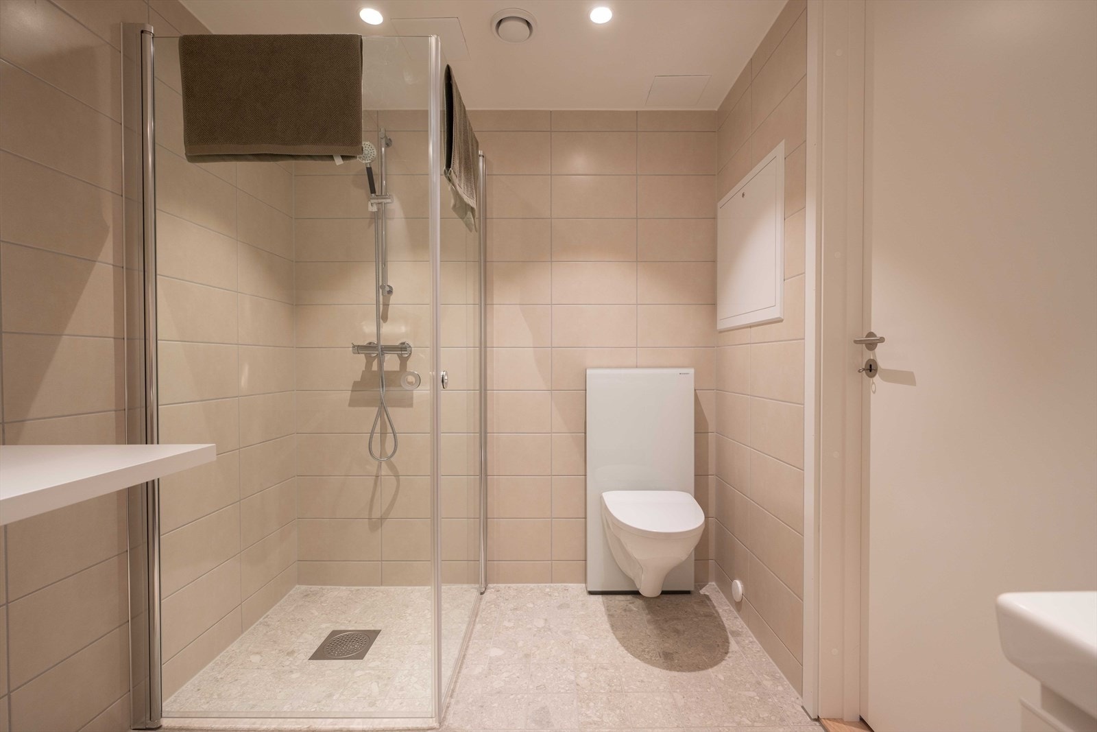 Delikat, flislagt bad med vegghengt toalett og dusjhjørne med innfellbare glassdører. Galleribilde