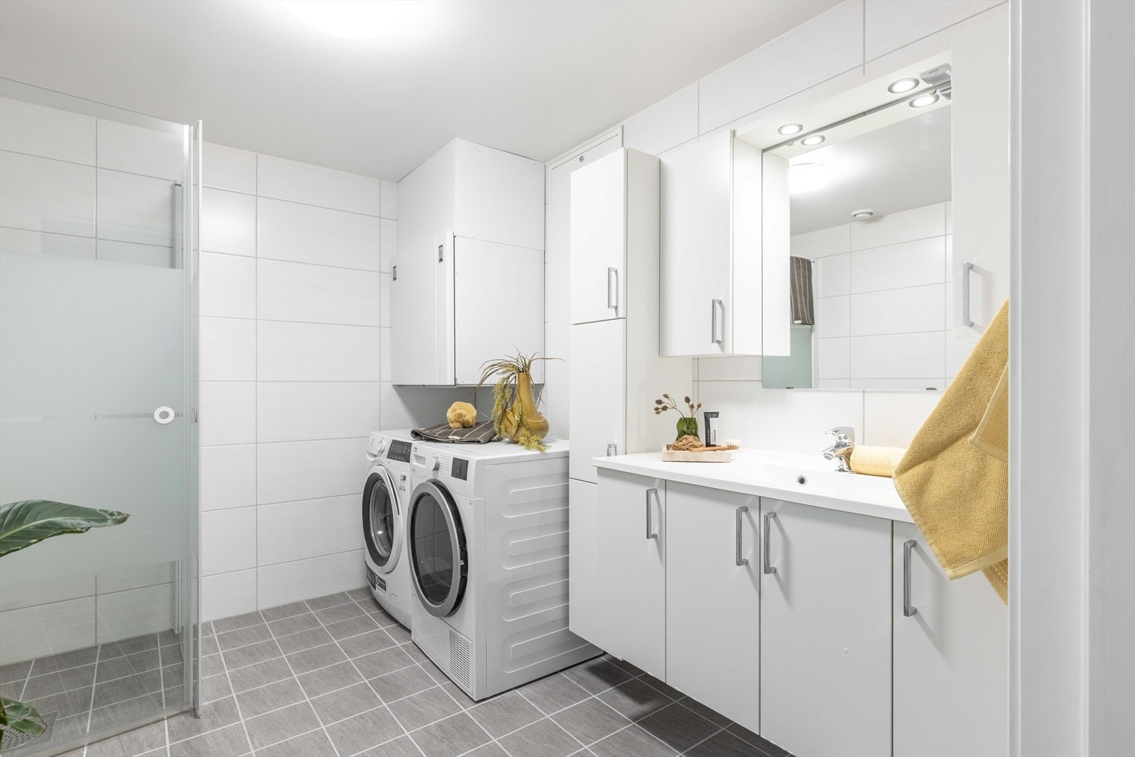 Her finner du baderomsinnredning med slette fronter, heldekkende servant med ett-greps blandebatteri, speil/skap med belysning, veggskap, ventilasjonsaggregat, vegghengt toalett og dusj med innfellbare dører i herdet glass. Galleribilde