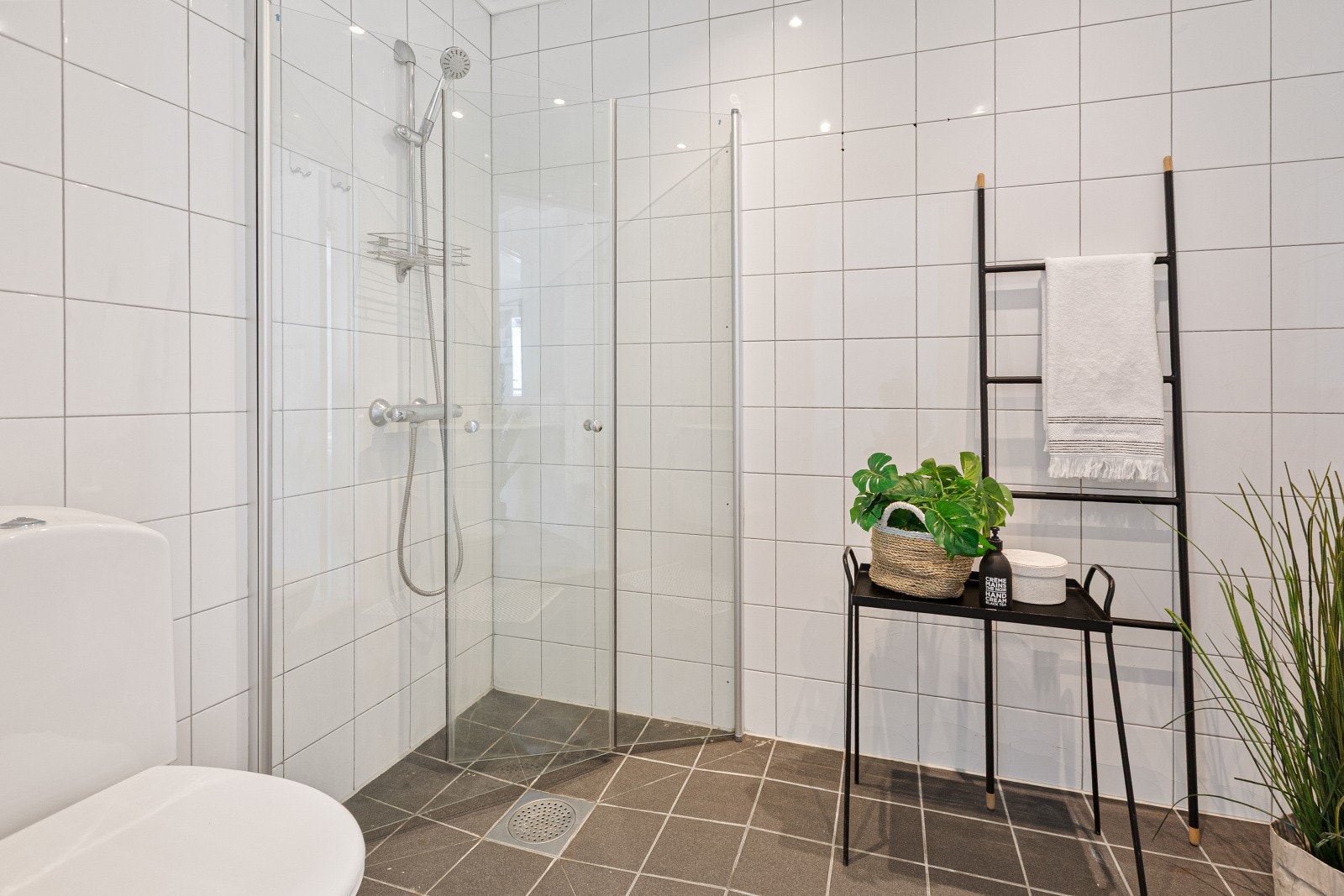 Rommet er innredet med hvit servantinnredning med praktisk skuffeseksjon, speil med belysning, gulvstående toalett og et pent dusjhjørne med glassdører. Gulvvarme. Galleribilde